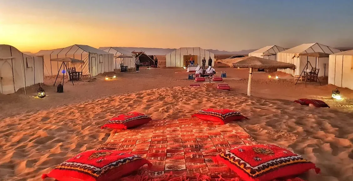 A serene desert scene featuring tents and colorful pillows arranged on the warm sand on our 2-Day Desert Tour from Marrakech to Zagora