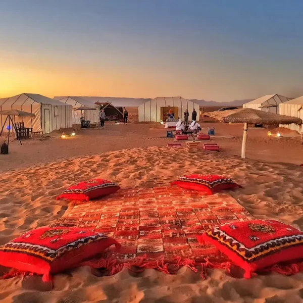 A serene desert scene featuring tents and colorful pillows arranged on the warm sand on our 2-Day Desert Tour from Marrakech to Zagora