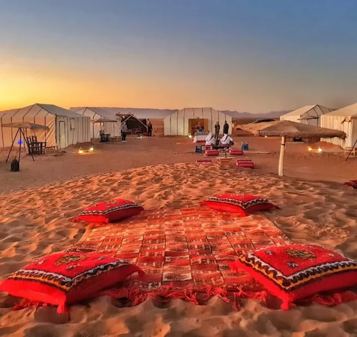 A serene desert scene featuring tents and colorful pillows arranged on the warm sand on our 2-Day Desert Tour from Marrakech to Zagora