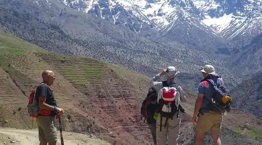 Three individuals with backpacks are positioned on a dirt road, surrounded by natural scenery.