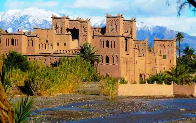 A large castle stands majestically with mountains in the background, representing the Best Morocco Private Tour Company.