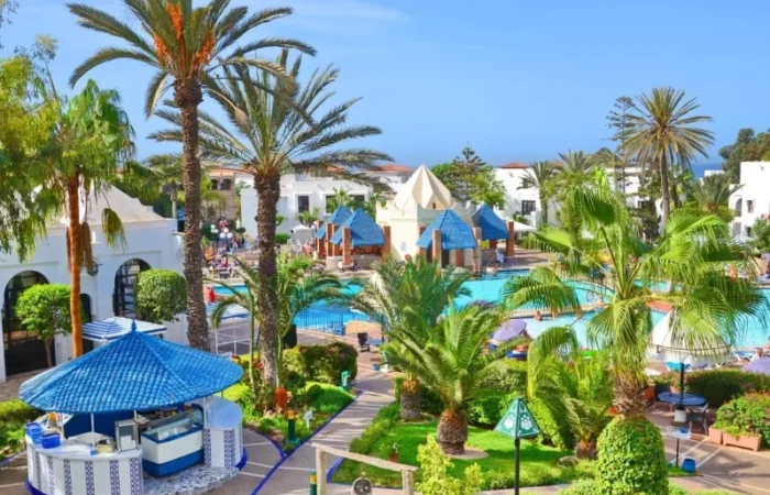 A luxurious resort in Morocco featuring a sparkling pool surrounded by lush palm trees, ideal for relaxation.