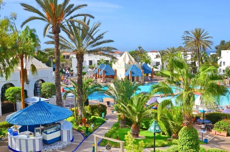 A luxurious resort in Morocco featuring a sparkling pool surrounded by lush palm trees, ideal for relaxation.
