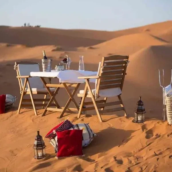A beautifully set dinner table in the Moroccan desert, surrounded by sand dunes under a starry sky.