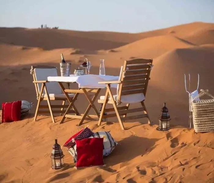 A beautifully set dinner table in the Moroccan desert, surrounded by sand dunes under a starry sky.