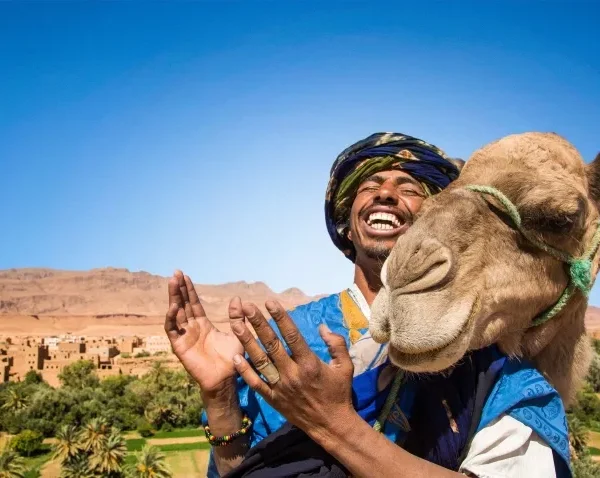 A man in a turban and blue dress holds a camel, promoting a Morocco trip package.