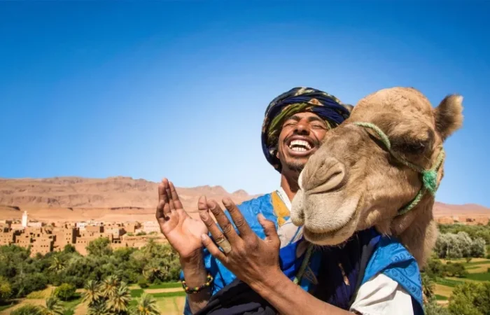 A man in a turban and blue dress holds a camel, promoting a Morocco trip package.