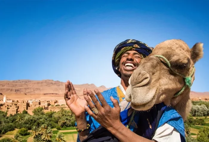 A man in a turban and blue dress holds a camel, promoting a Morocco trip package.