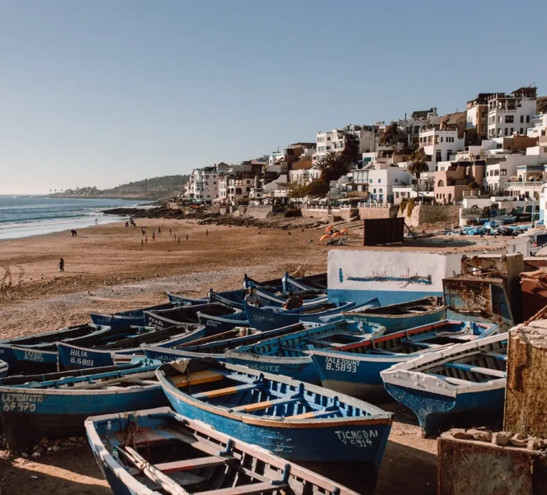 Blue and white boats lined up on the beach, with the ocean in the background, capturing the essence of Morocco surf travel.