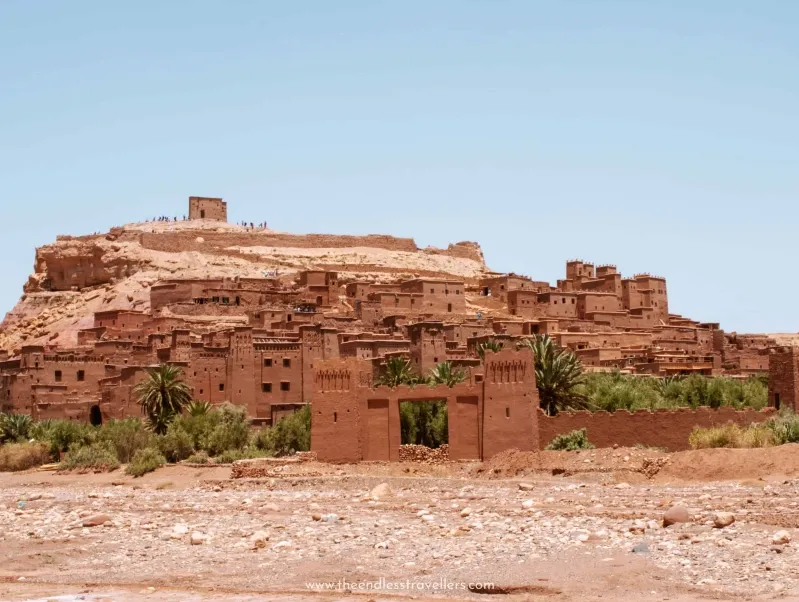 Ancient fortified village with earthen buildings and a gate, set on a hill with sparse vegetation under a clear sky.While Morocco 7 day itinerary