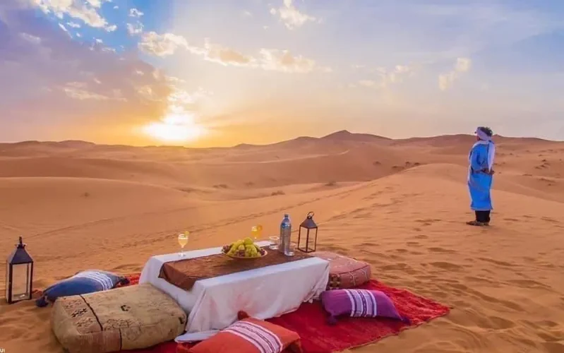 A romantic dinner set against a vibrant Sahara Desert sunset, showcasing the beauty of Morocco's landscapes.