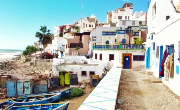 A scenic beach view with blue boats in the background, featured in a Morocco vacation travel guide.