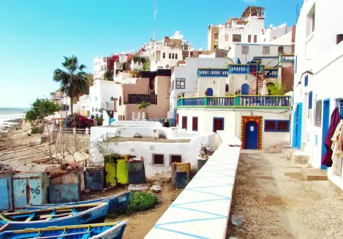 A scenic beach view with blue boats in the background, featured in a Morocco vacation travel guide.