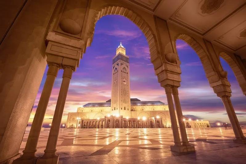 A mosque illuminated at sunset, set against the backdrop of the Moroccan Desert, showcasing vibrant colors in the sky.