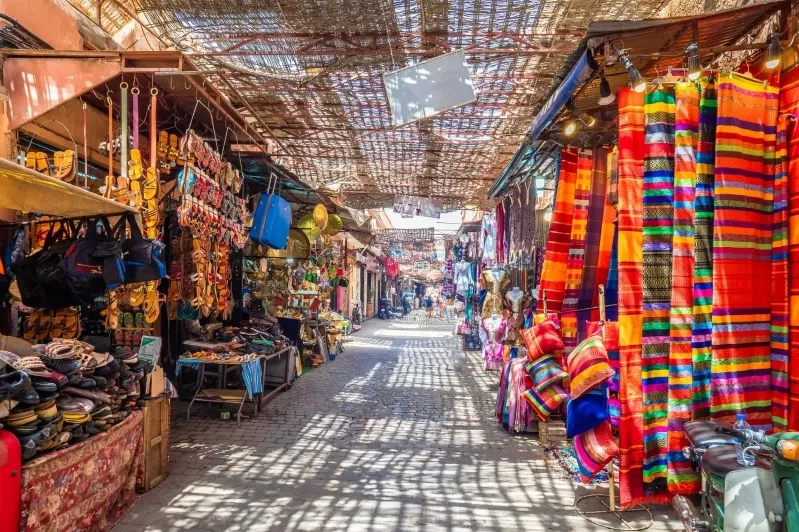 A narrow Moroccan street lined with vibrant cloths and various items, showcasing local culture and craftsmanship.
