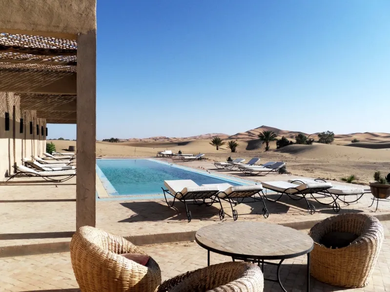 A serene pool surrounded by palm trees at a Moroccan desert resort, inviting relaxation in a tranquil setting. 