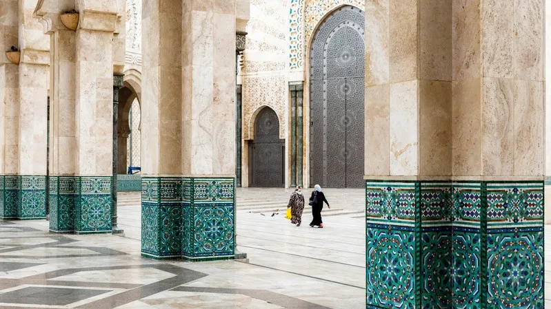 A man and woman stroll through the ornate halls of a mosque during their Moroccan travel experience.