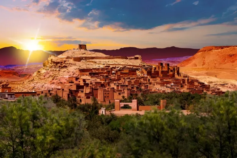 The sun sets over the city of Atad, Morocco, showcasing vibrant colors in the sky, perfect for a tour company promotion. 