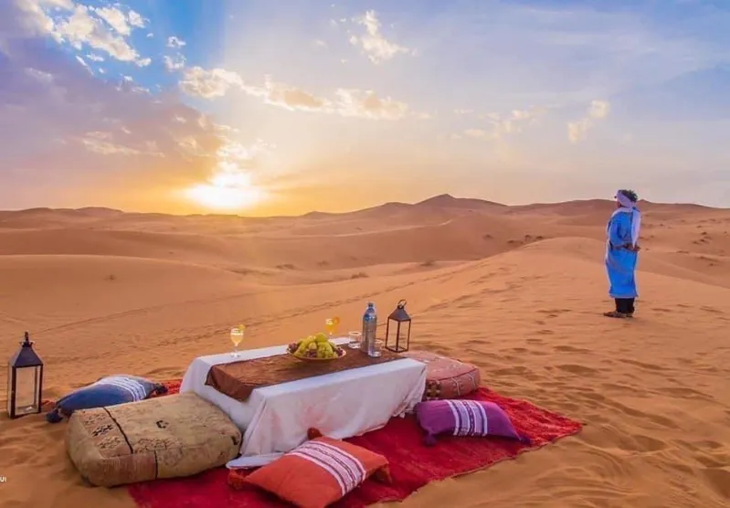 A romantic dinner set against a vibrant Sahara Desert sunset, highlighting Morocco Tour Packages.