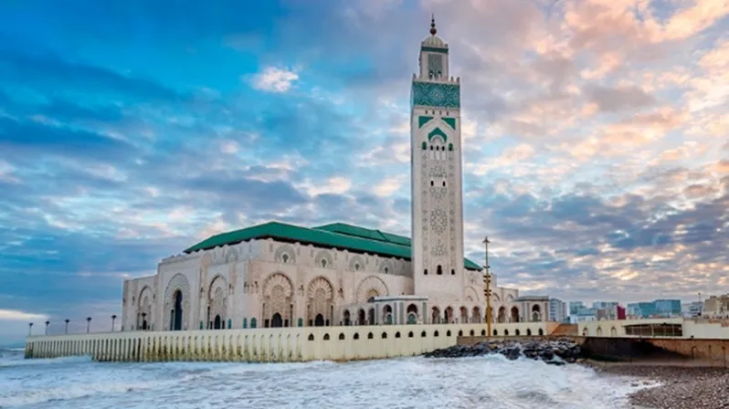 A mosque on the beach at sunset, showcasing its silhouette against the vibrant sky, a must-see in Casablanca.
