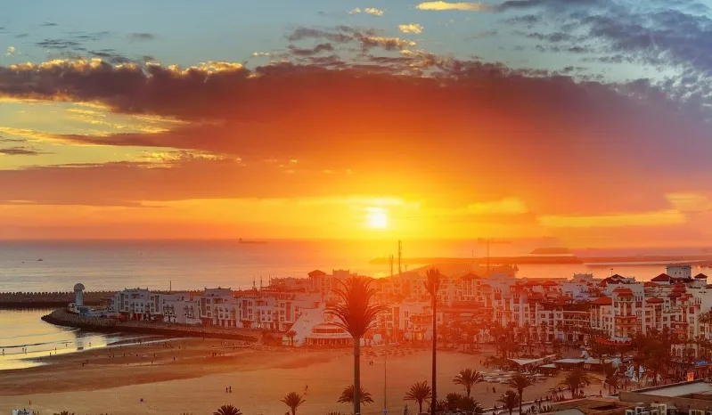 A vibrant sunset casts golden hues over Agadir's beach and city skyline, inviting visitors to enjoy the scenic view.