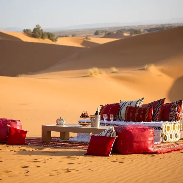 A table and chairs with red cushions set in the Moroccan desert, showcasing a serene outdoor dining experience.