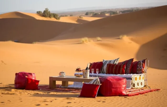 A table and chairs with red cushions set in the Moroccan desert, showcasing a serene outdoor dining experience.