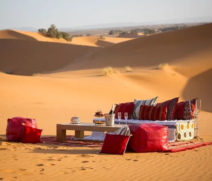 A table and chairs with red cushions set in the Moroccan desert, showcasing a serene outdoor dining experience.
