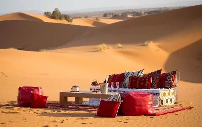 A table and chairs with red cushions set in the Moroccan desert, showcasing a serene outdoor dining experience.