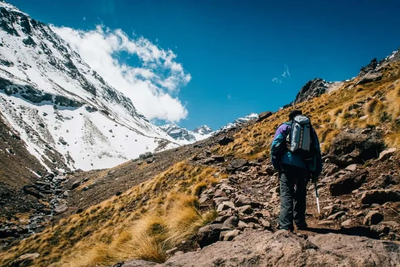 A man with a backpack hiking up a mountain, showcasing the beauty of Morocco's guided tours in nature.