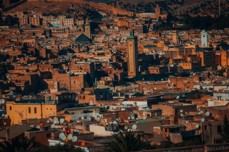 A panoramic view of Marrakech, Morocco, showcasing its vibrant architecture and bustling streets, with a camel trek in the foreground.