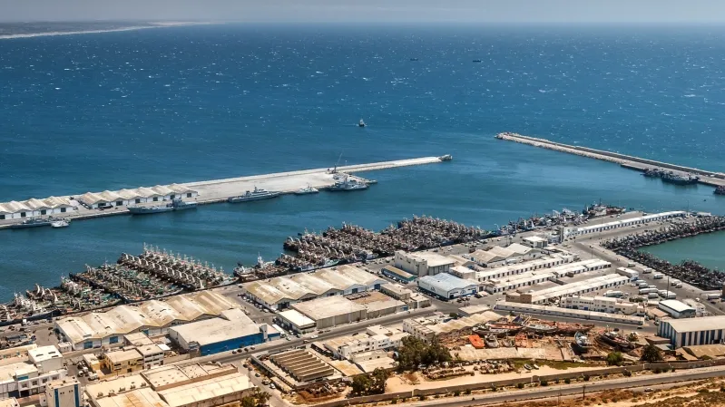 Aerial view of the port of Israel, showcasing shipping containers and vessels, with the coastline in the background.