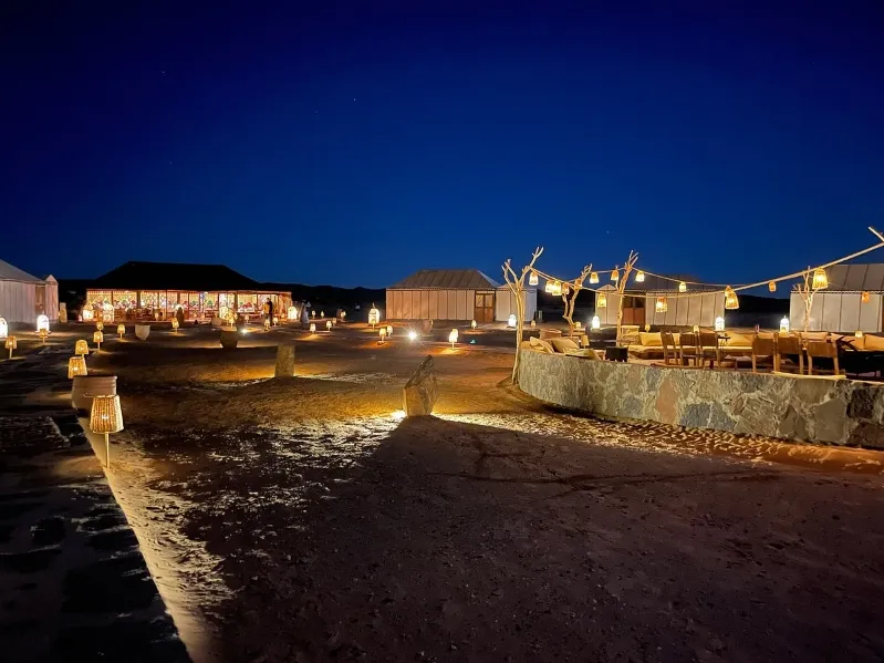 A serene night view of a beach featuring a few illuminated huts, highlighting the beauty of luxury tours in Morocco.