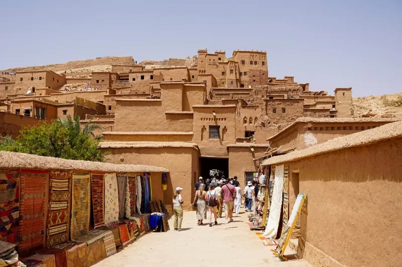 People walk through a narrow desert alleyway, showcasing the unique architecture of Morocco.