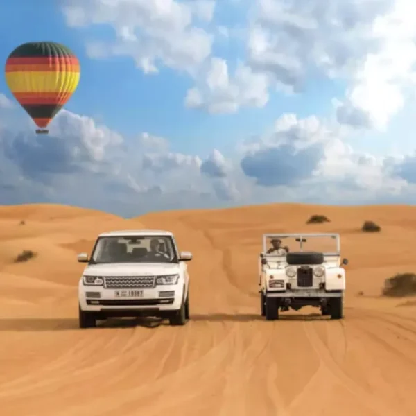 Two vehicles drive through a desert landscape with a colorful hot air balloon floating in the background, promoting Morocco custom tours.