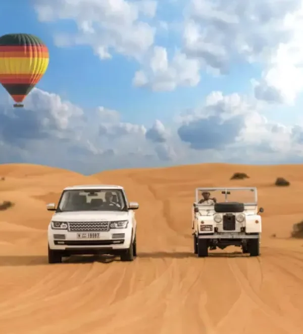 Two vehicles drive through a desert landscape with a colorful hot air balloon floating in the background, promoting Morocco custom tours.