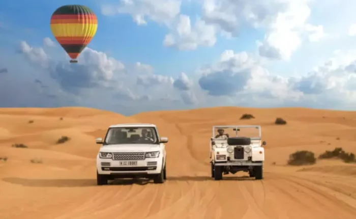 Two vehicles drive through a desert landscape with a colorful hot air balloon floating in the background, promoting Morocco custom tours.