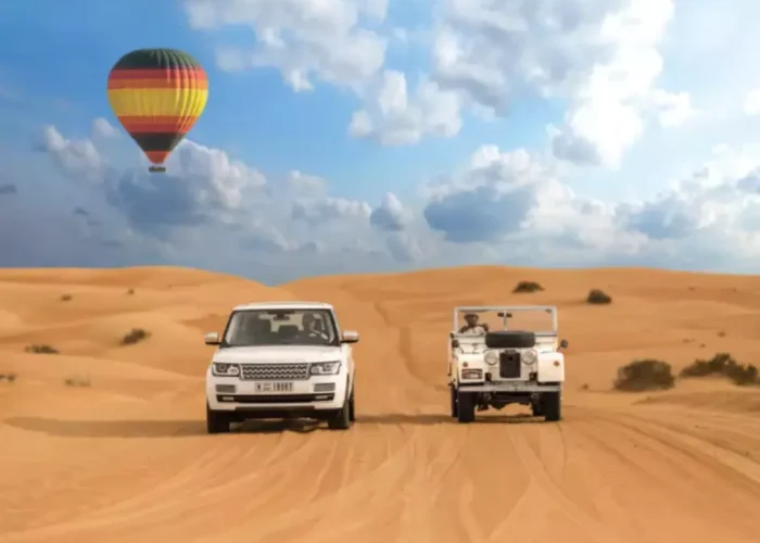 Two vehicles drive through a desert landscape with a colorful hot air balloon floating in the background, promoting Morocco custom tours.