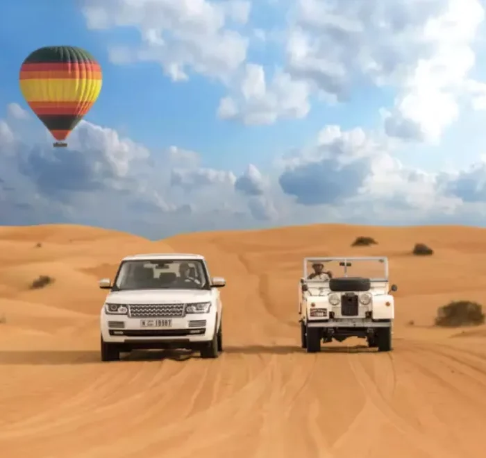 Two vehicles drive through a desert landscape with a colorful hot air balloon floating in the background, promoting Morocco custom tours.