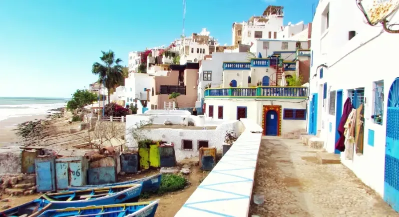 A scenic beach view with blue boats in the background, promoting guided trips to Morocco.