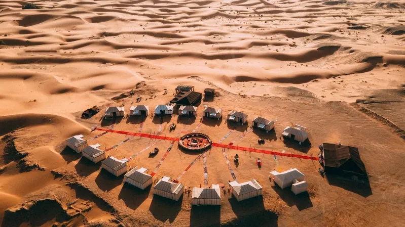 Aerial view of a desert camp in Morocco, featuring several tents set up for a camel trek adventure.