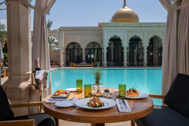 A beautifully set table with food and drinks beside a sparkling pool, showcasing Morocco luxury travel.