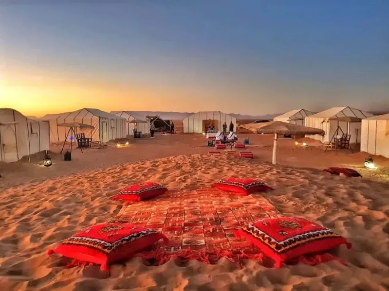 A desert camp in Morocco featuring tents and colorful pillows arranged on the sand for a guided tour experience.