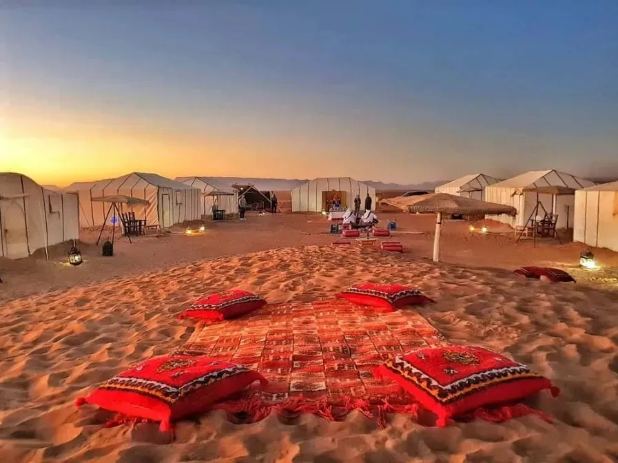 A desert camp in Morocco featuring tents and colorful pillows arranged on the sand, ideal for travel tours.