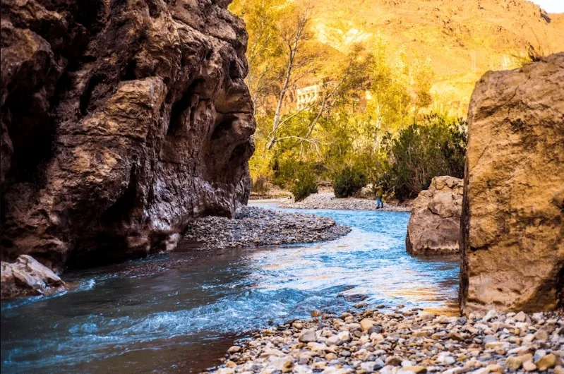 A river flows through a mountainous canyon, showcasing the natural beauty encountered on the Marrakech to Fes Desert Tour. 