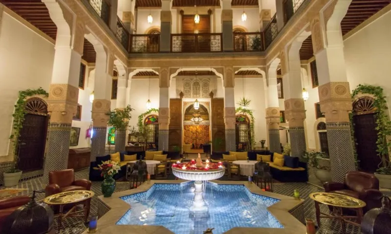 Interior view of a luxury hotel featuring a decorative fountain and a serene swimming pool, ideal for Morocco Tours.