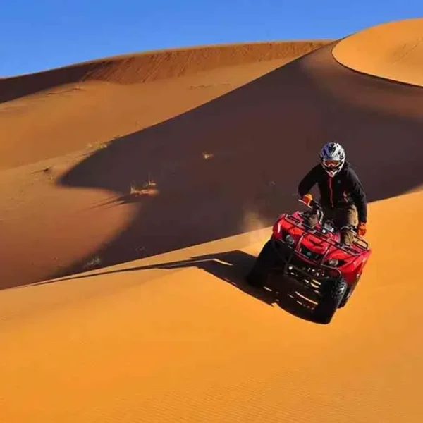 A man riding an ATV through the desert during the Marrakech to Fes Desert Tour, with sand dunes in the background.