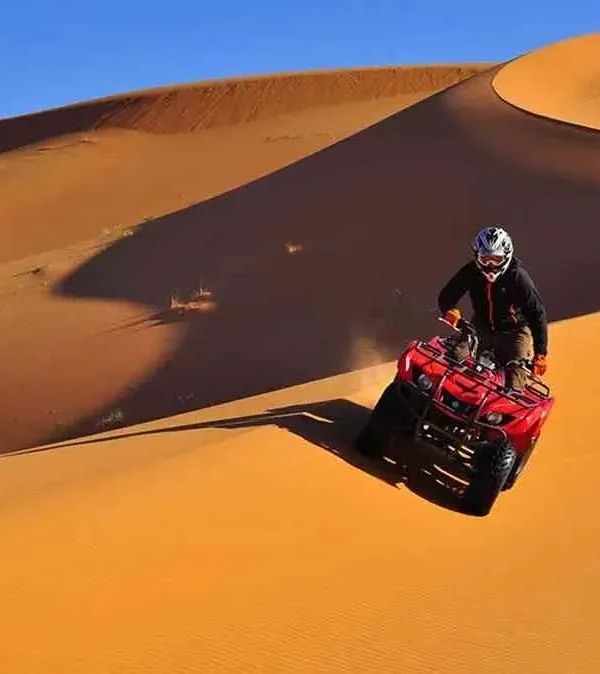 A man riding an ATV through the desert during the Marrakech to Fes Desert Tour, with sand dunes in the background.