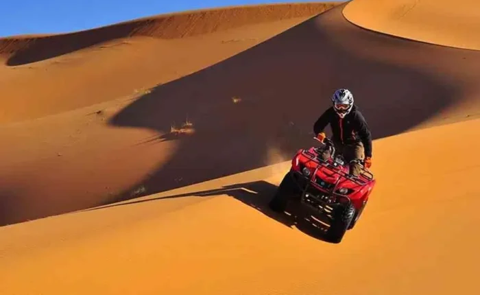 A man riding an ATV through the desert during the Marrakech to Fes Desert Tour, with sand dunes in the background.