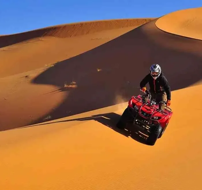 A man riding an ATV through the desert during the Marrakech to Fes Desert Tour, with sand dunes in the background.